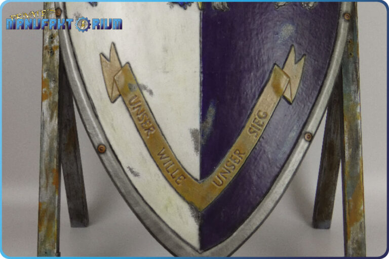 Detailansicht vom unteren Bereich des LARP Schild Löwe und Greif. Auf dem pergamentfarbigen Schriftband steht der zweite Teil des Wahlspruchs "Unser Wille Unser Sieg"